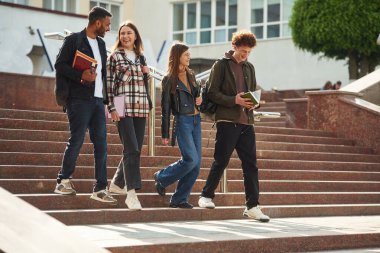 Merdivenlerden iniyorum. Gündelik giysiler içinde dört genç dışarıda beraberler..