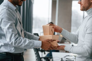 Yandan bak. Karton ekolojik kutular tutuyor. İki adam modern ofiste birlikte çalışıyor..