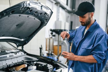 Yağ tenekesi ellerinde. Otomobil tamircisi garajda çalışıyor. Onarım servisi.