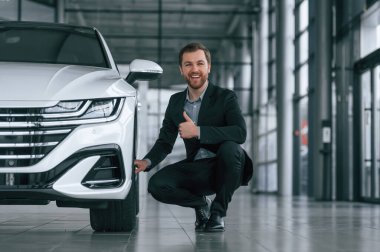 Oturup başparmağını kaldırıyorsun. Siyah takım elbiseli adam otomobilin yanındaki araba galerisinde..