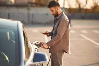 Yeşil enerji kavramı. Adam dışarıda elektrikli arabasının yanında duruyor..