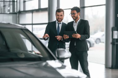 Gri renkli otomobilin yanında. İki işadamı araba galerisinde birlikte çalışıyorlar..