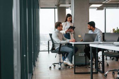 Gülümsüyor ve konuşuyor. Erkekler ve kadınlar ofiste birlikte çalışıyorlar..