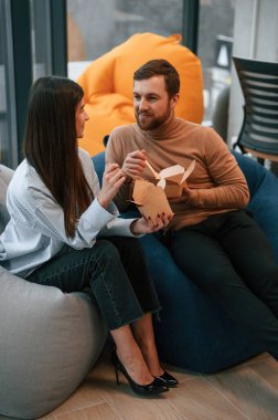 Oturup konuşmak. Ofis çalışanları dinlenme alanındalar ve kağıt eko kutulardan yemek yiyorlar..