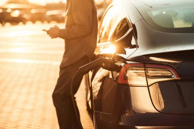 Güzel güneş ışığı. Adam dışarıda elektrikli arabasının yanında duruyor..