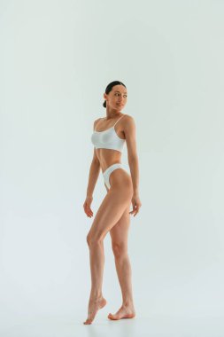 Beyaz spor kıyafetleri içinde. Stüdyoda zayıf vücutlu genç bir kadın var..