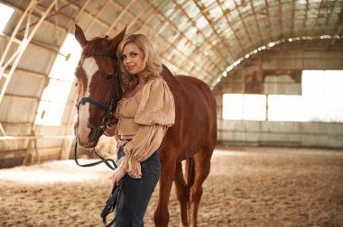 Güneşli bir gün. Hayvanın yanında durmak. Güzel genç bir kadın atıyla içeride..