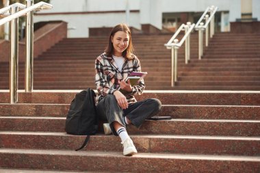 Genç kız öğrenci üniversitenin merdivenlerinde oturuyor..