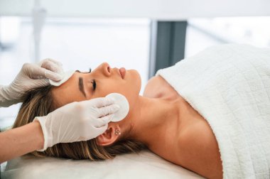 Pamuk ped ya da sünger kullanarak cilt temizleme. Kadın yüzü güzellik salonunda güzellik uzmanları tarafından tedavi ediliyor..