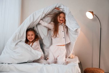 Yatak odasında, ellerinde battaniyeyle. İki küçük kız evcil odada oynuyorlar ve eğleniyorlar..