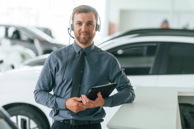 Müdür kulaklıkla ve not defteriyle birlikte. Yakışıklı araba galerisi çalışanı elektrikli araçla çalışıyor..