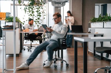 Tabletle birlikte sandalyede. Erkekler ve kadınlar ofiste birlikte çalışıyorlar..