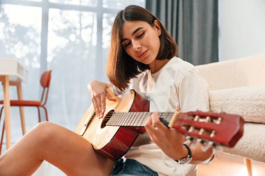 Elinde klasik gitarla. Günlük giysiler içinde güzel bir kadın evde, yurt odasında..