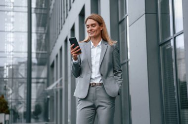 Boş zaman, yürümek, akıllı telefon tutmak. Resmi giysili kadın iş binasının yakınında dışarıda..
