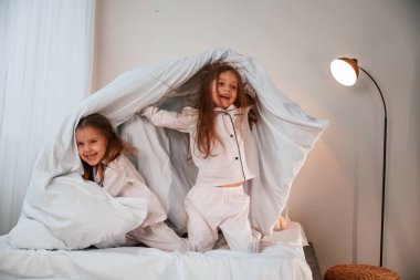 Yatak odasında, ellerinde battaniyeyle. İki küçük kız evcil odada oynuyorlar ve eğleniyorlar..