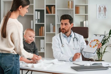 Sağlıklı yemekten bahsediyorum. Bebek ve anneyle. Resmi kıyafetli doktor dolapta çalışıyor..