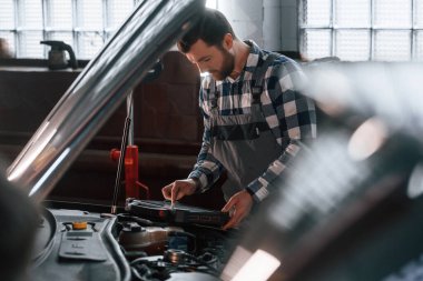 Arabanın kaputu açıldı. Tablet kullanıyorum. Üniformalı adam araba galerisinde çalışıyor..