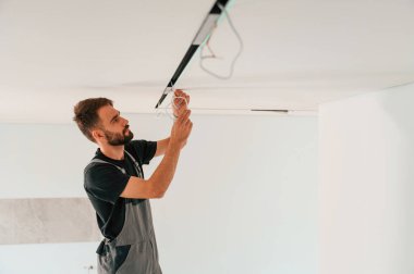 Tavana ışıklandırma ekipmanı kuruluyor. Adam iç mekanda çalışıyor..