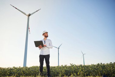 Ayakta ve dizüstü bilgisayar kullanarak. Servis mühendisi yel değirmenleriyle sahada..