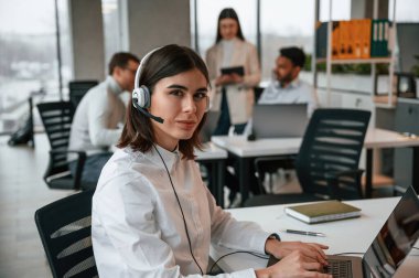 Kadın dizüstü bilgisayarla çalışıyor. Ofiste birlikte çalışan dört kişi var..
