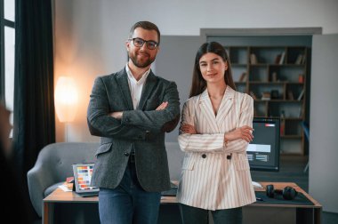Kollarını kavuşturmuş duruyorsun. Modern ofiste iki çalışan birlikte çalışıyor..