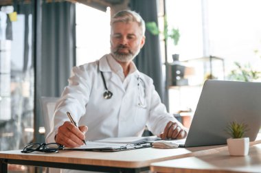 Belgeye bilgi yazılıyor. Beyaz önlüklü kıdemli doktor içeride çalışıyor..