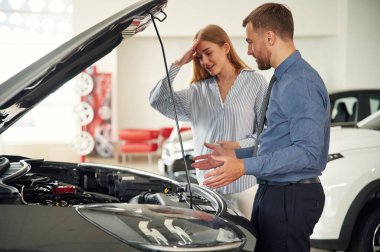 Kaputun altında. Resmi elbiseli adam elektrikli arabalı kadın müşteriyle birlikte..