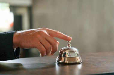 Otel masasının zilini kullanarak manzarayı kapat. Otel resepsiyonunda siyah ceketli bir adam var..