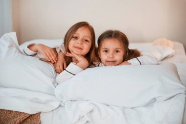 Gülümsüyor, yatağa uzanıyor. İki küçük kız evcil odada oynuyorlar ve eğleniyorlar..