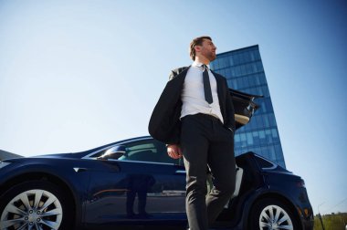 Aşağıdan bak. Kapılar açıldı. İş adamı dışarıda arabasının yanında duruyor..