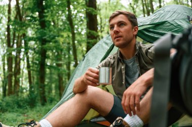Bir bardak suyla. Çadırın yanında oturuyor. Yaz ormanında bir turist. Keşif ve eğlence kavramı.