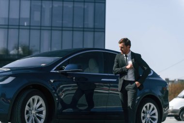 Ayakta, siyah takım elbiseli. İş adamı arabasının yanında..