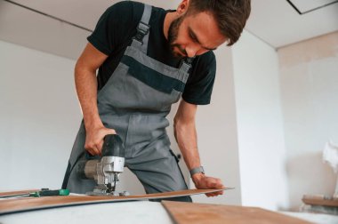 Tahtayı kesmek için elektrikli makineyi kullanmak. Adam yeni kaplamalı ahşap döşeme kuruyor..
