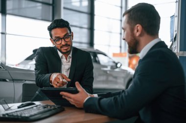 Masanın yanında oturuyor. İki işadamı araba galerisinde birlikte çalışıyorlar..