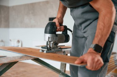 Tahtayı kesmek için elektrikli makineyi kullanmak. Adam yeni kaplamalı ahşap döşeme kuruyor..