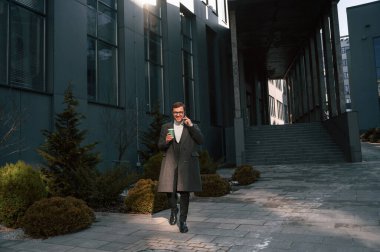 Bir bardak içki ve akıllı telefonla. Resmi kıyafetli yakışıklı dışarıda, iş binasının yanında..