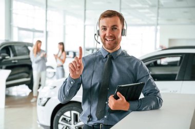 Müdür kulaklıkla ve not defteriyle birlikte. Yakışıklı araba galerisi çalışanı elektrikli araçla çalışıyor..