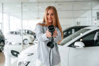 Gülümseyen ve elektrikli araba için şarj cihazı tutan. Güzel kadın içeride..