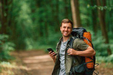 Büyük bir sırt çantası ve akıllı telefon. Yaz ormanında bir turist. Keşif ve eğlence kavramı.