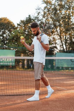 Ağın yanında raketle bekliyorum. Genç adam güneşli bir günde tenis kortunda..