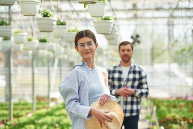 Hasır şapkalı bir kadın. Çiçekçi adam parlak serada çalışıyor..