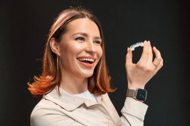 Genç bir kadın siyah arka plana karşı duruyor ve hizalayıcıyı tutuyor..