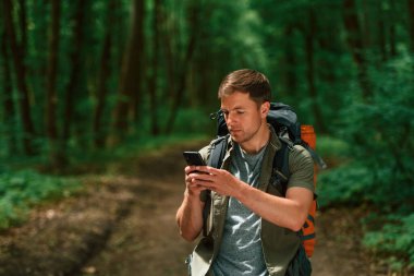 Büyük bir sırt çantası ve akıllı telefon. Yaz ormanında bir turist. Keşif ve eğlence kavramı.