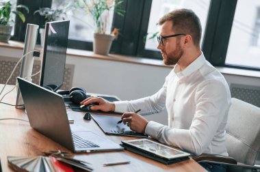 Yan görüş. Resmi kıyafetli adam modern ofiste çalışıyor. Bilgisayar kullanılıyor.