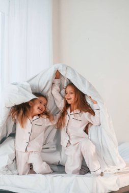 Yatağın üzerindeki battaniyenin altında. İki küçük kız evcil odada oynuyorlar ve eğleniyorlar..