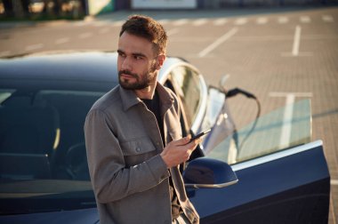 Otomobili şarj ediyorum. Adam dışarıda elektrikli arabasının yanında duruyor..