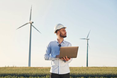 Ellerinde dizüstü bilgisayarla. Servis mühendisi yel değirmenleriyle sahada..