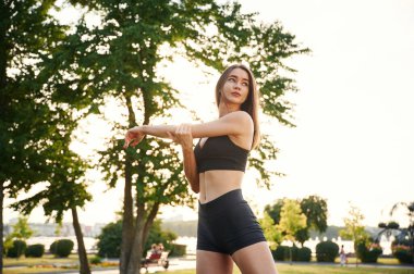 Egzersizler, ağaç ve gökyüzüne karşı. Spor elbiseli güzel bir kadın güneşli bir günde parkta..