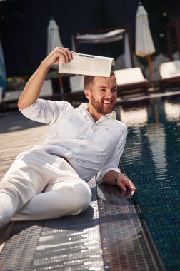 Elinde gazete tutuyor. Resmi giyinmiş yakışıklı adam havuzda..