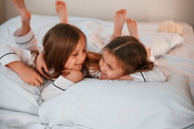 Gülümsüyor, yatağa uzanıyor. İki küçük kız evcil odada oynuyorlar ve eğleniyorlar..